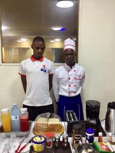 Dos hombres están parados junto a una mesa con comida. en Shangri-La Fortune Hotel en Kampala