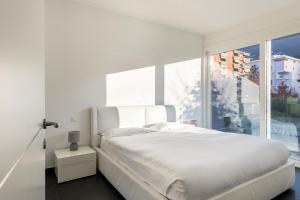- une chambre avec un lit blanc et une grande fenêtre dans l'établissement Roggia Apartments by Quokka 360 - central flats with parking space, à Lugano