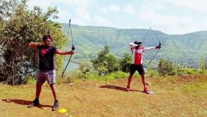 two young men are playing with arrows on a hill at I-Camp Resort in Mahabaleshwar