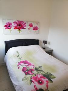 a bed with a white blanket with pink flowers on it at logement entier au calme in Villers-Outréaux