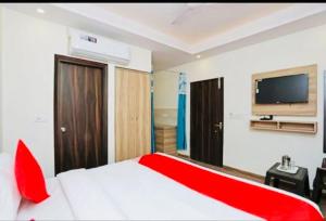 Airport Hotel Golden Bliss Near Delhi Airport في نيودلهي: غرفة نوم بسرير احمر وبيض وتلفزيون بشاشة مسطحة