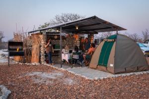 een groep mensen die aan een tafel onder een tent zitten bij Etosha Trading Post Campsite in Okaukuejo