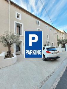 um sinal de estacionamento com um carro estacionado em frente a um edifício em Maison 1634 - Centre historique, parking, petit-dejeuner compris, climatisation, piscine em Pézenas
