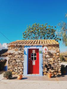 una pequeña casa con puerta roja y pared de piedra en Quinta do Sardanito de Tras, en Zambujeira do Mar
