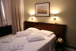 Una cama con dos almohadas blancas y un teléfono. en Golden Ingá Hotel en Maringá