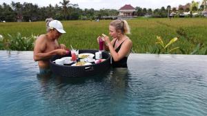 Ein Mann und eine Frau essen im Wasser. in der Unterkunft Paraiso Cottage Ubud in Ubud