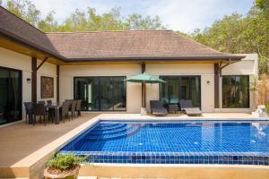 ラワイビーチにあるQueen Palm Villaの家の隣に椅子とパラソル付きのプールがあります。