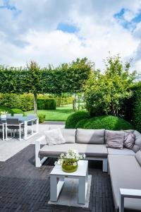 un patio con sofás blancos, mesas y árboles en B&B La Cereza, en Oudenaarde