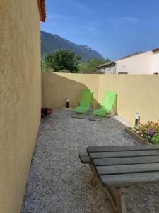 - 2 chaises vertes et un banc sur la terrasse dans l'établissement Studio les trois chemins, à Cucugnan