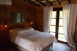 um quarto com uma cama com lençóis brancos e uma janela em POUSADA PARAISO DOS TUCANOS em Aiuruoca