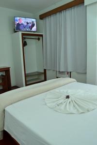 a bedroom with a white bed with a tv on the wall at Hotel Dias - By UP Hotel in Pouso Alegre