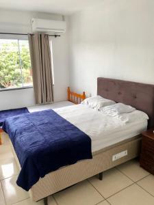 a bedroom with a bed with a blue blanket and a window at Residencial Sandini Garopaba in Garopaba