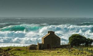 an old building on the beach with a large wave at Ostán Oileán Thoraí Tory Island Hotel in Tory Island