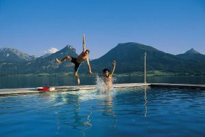 ザンクト・ヴォルフガングにあるRomantik Hotel Im Weissen Rössl am Wolfgangseeの水中のスイミングプールに飛び込む2名