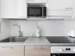 eine weiße Küche mit einer Spüle und einer Mikrowelle in der Unterkunft Kotimaailma Apartments Joensuu - Kalevankatu 36 in Joensuu