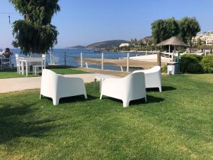 two white chairs sitting on the grass near the beach at Gumbet Cove Hotel in Gümbet