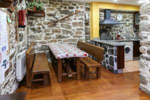 cocina con mesa, sillas y pared de piedra en 4 bedrooms house with jacuzzi furnished garden and wifi at Tineo, en Tineo