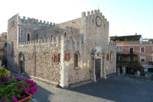 un grande edificio in pietra con un orologio sopra di Casa Girolamo in Piazza Duomo a Taormina