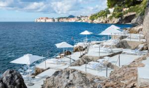 a group of white chairs and umbrellas on a beach at Villa Dubrovnik in Dubrovnik