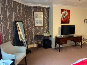 a living room with a television and a desk with a chair at The Kingswood Guest House - Adult Only in Weymouth
