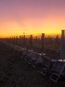 a line of chairs and umbrellas on the beach at sunset at Hotel Savoia in Lido di Jesolo