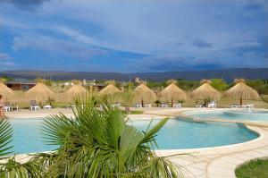 um resort com uma piscina com cadeiras e guarda-sóis de palha em Arenas Blancas Cabañas & Suites em Nono