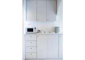 a white kitchen with white cabinets and a microwave at K Hotel Aliwal (Premier) in Singapore