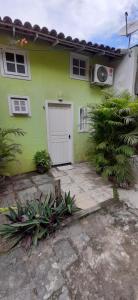 a green house with a white door and some plants at Loft e Vila da Praia Studios Ilha Grande in Abraão