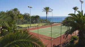 a tennis court with palm trees and the ocean at SBH Club Paraiso Playa in Playa Jandia