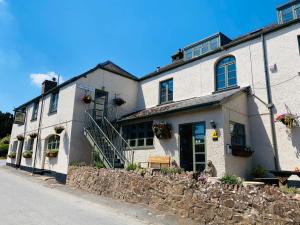 a white building with a stone wall next to a street at The Royal Oak Inn in Withypool