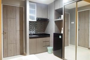 a kitchen with wooden cabinets and a black refrigerator at Modern Spacious Studio Room Apartment at Taman Melati Surabaya By Travelio in Surabaya