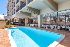 a swimming pool in front of a building with tables and chairs at The Plaza Hotel Kalgoorlie in Kalgoorlie