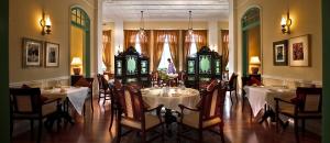 un comedor con mesas y sillas blancas y ventanas en The Majestic Malacca Hotel - Small Luxury Hotels of the World en Melaka