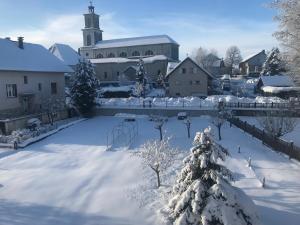 a snow covered yard with a church and a christmas tree at Meublé de tourisme in Frasne