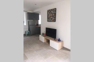 Una sala de estar con un televisor de pantalla plana en una pared blanca. en Maison bord de Mer, en Bernières-sur-Mer