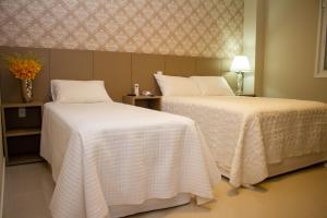 two beds in a hotel room with white sheets at Hotel Seville Comfort in Telêmaco Borba