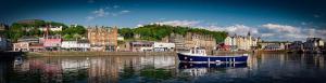 a blue boat sitting in the water near a city at McCaig's Tower Apartment in Oban