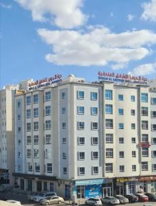 درة الخوير للشقق الفندقيه في مسقط: مبنى ابيض كبير به سيارات تقف في موقف للسيارات
