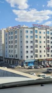 a large white building with cars parked in a parking lot at درة الخوير للشقق الفندقيه in Muscat