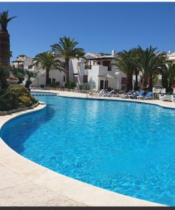 a large blue swimming pool with chairs and palm trees at Dafne's Beach in La Pineda