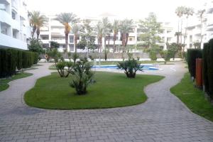 een loopbrug door een park met palmbomen en een gebouw bij Bonito apartamento de 3 hab. con jardín in Roses