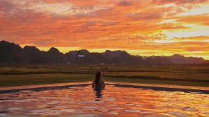uma mulher sentada numa piscina infinita ao pôr-do-sol em Karst Villas Phong Nha em Phong Nha
