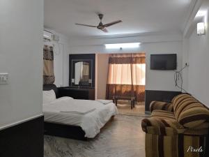 a bedroom with a bed and a couch and a tv at Sai Pavilion in Puttaparthi
