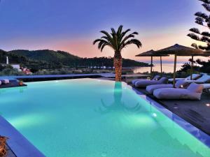 a swimming pool with lounge chairs and a palm tree at Panormos Beach Hotel Skopelos in Panormos Skopelos