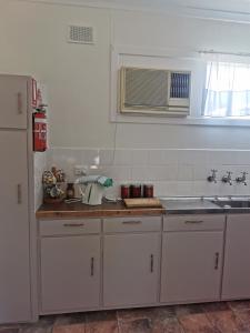 una cucina con armadi bianchi, lavandino e frigorifero di Kimba Units a Kimba