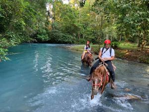 dos personas montando caballos a través de un río en Hotel SueñoReal RioCeleste, en Rio Celeste
