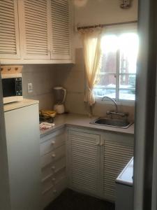 kuchnia z białymi szafkami, umywalką i oknem w obiekcie Piriapolis apartamento w mieście Piriápolis