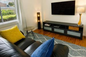 a living room with a black leather couch and a flat screen tv at Ascot Road - discover Bowral in Bowral