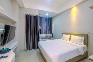 a bedroom with a white bed and a television at Homey and Warm Studio Apartment Oasis Cikarang By Travelio in Cikarang +8 photos