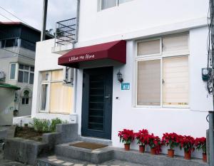 een wit gebouw met een zwarte deur en rode bloemen bij 李家出走民宿 in Sanzhi
